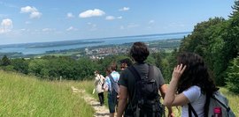 Von hinten sind die Teilnehmer*innen beim Wandern, mit Blick auf den Chiemsee fotografiert.